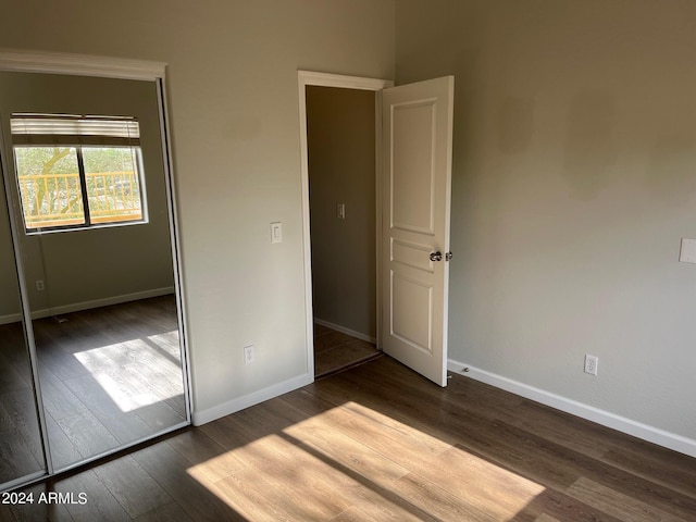 unfurnished bedroom with dark wood-style floors, a closet, and baseboards