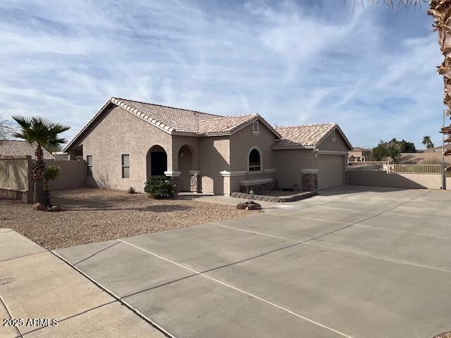 mediterranean / spanish-style home featuring a garage, fence, driveway, a tiled roof, and stucco siding