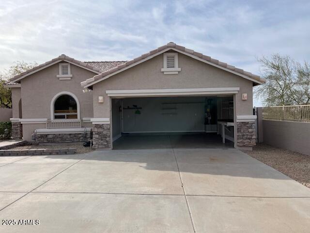 view of front facade featuring an attached garage, fence, stone siding, driveway, and stucco siding