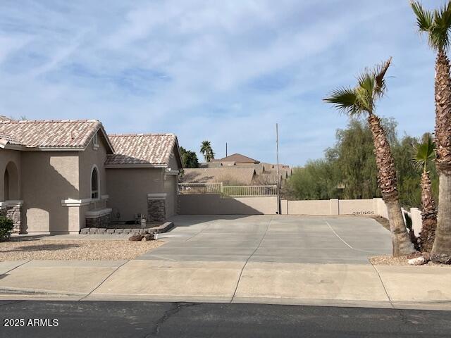 view of side of property with a tile roof, fence, concrete driveway, and stucco siding