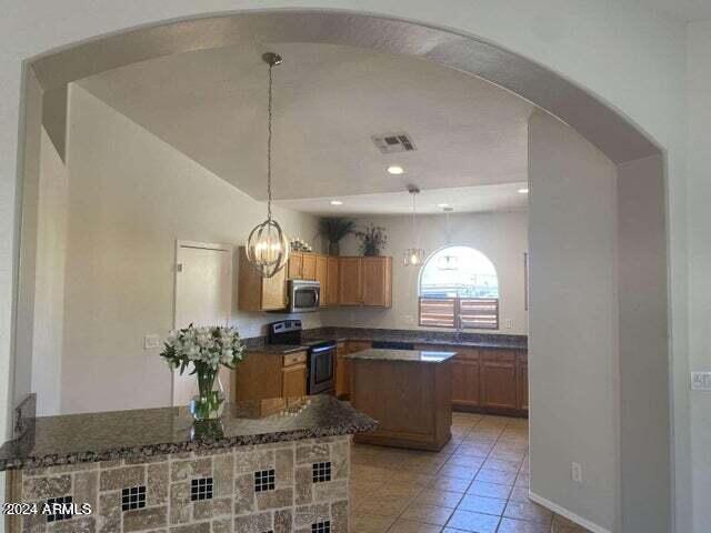 kitchen featuring visible vents, arched walkways, a kitchen island, stainless steel appliances, and light tile patterned flooring