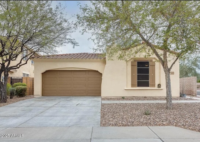 mediterranean / spanish-style home with fence, stucco siding, concrete driveway, a garage, and a tile roof