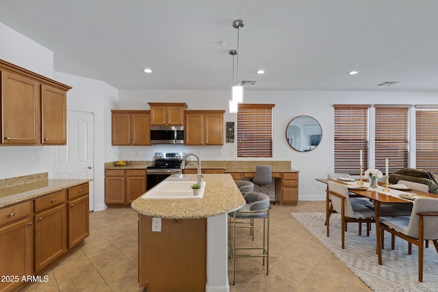 kitchen featuring pendant lighting, stainless steel appliances, a center island with sink, a kitchen bar, and sink