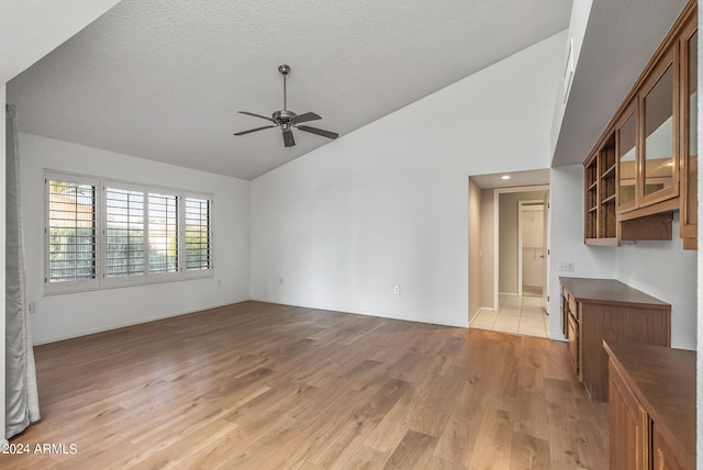 unfurnished living room featuring lofted ceiling, light hardwood / wood-style floors, a textured ceiling, and ceiling fan