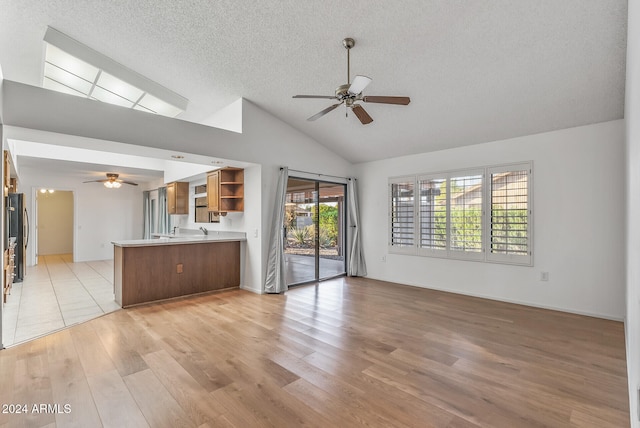 unfurnished living room with ceiling fan, a textured ceiling, light hardwood / wood-style flooring, and high vaulted ceiling