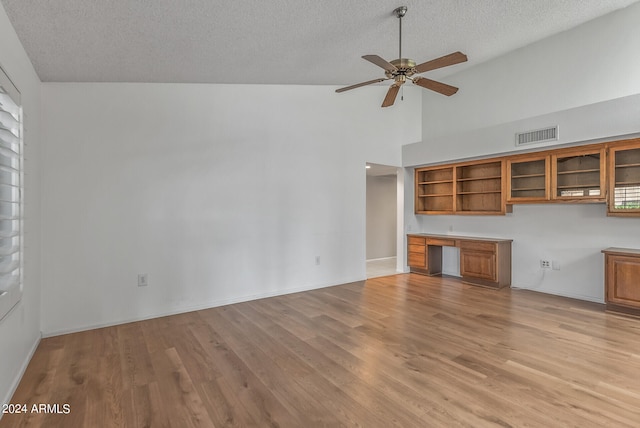 unfurnished living room with high vaulted ceiling, built in desk, light hardwood / wood-style floors, and a textured ceiling