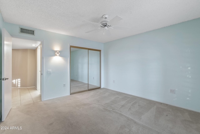 unfurnished bedroom featuring ceiling fan, a textured ceiling, a closet, and light carpet