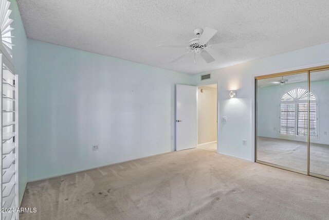 unfurnished bedroom with light carpet, ceiling fan, a closet, and a textured ceiling