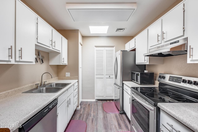 kitchen with appliances with stainless steel finishes, a skylight, sink, hardwood / wood-style flooring, and white cabinets