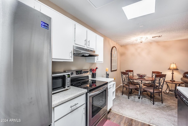 kitchen with hardwood / wood-style floors, white cabinets, a skylight, a textured ceiling, and appliances with stainless steel finishes