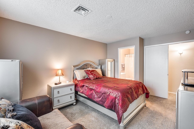 bedroom with ensuite bathroom, light carpet, and a textured ceiling