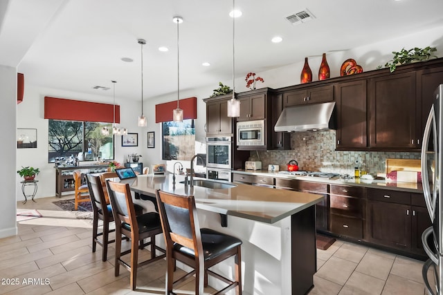 kitchen featuring hanging light fixtures, backsplash, an island with sink, a breakfast bar area, and stainless steel appliances