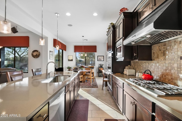 kitchen with wall chimney exhaust hood, sink, backsplash, decorative light fixtures, and stainless steel appliances