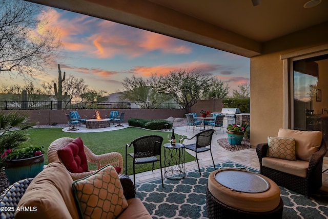 patio terrace at dusk with area for grilling, a yard, and an outdoor living space with a fire pit