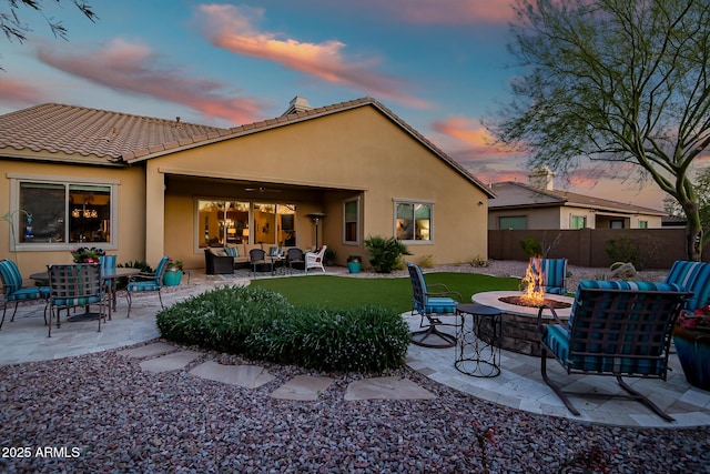 back house at dusk with an outdoor living space with a fire pit, a lawn, and a patio