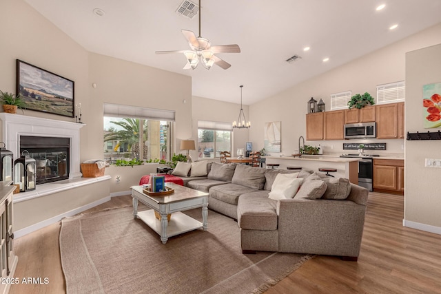 living room with ceiling fan with notable chandelier, high vaulted ceiling, and hardwood / wood-style floors