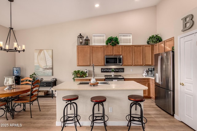 kitchen featuring appliances with stainless steel finishes, hanging light fixtures, an island with sink, a kitchen bar, and light wood-type flooring