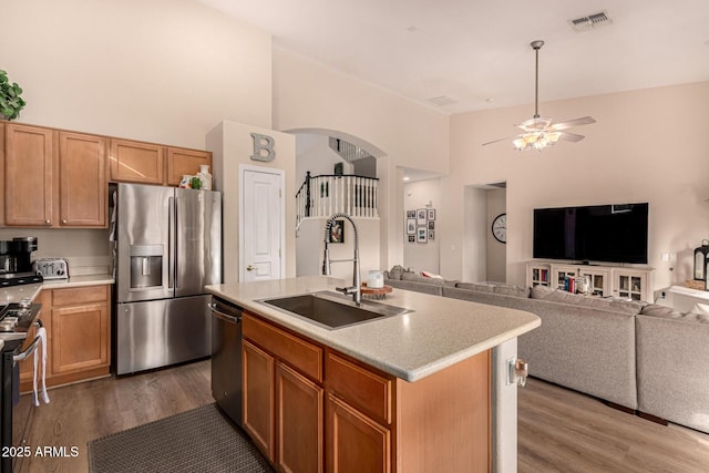 kitchen featuring wood-type flooring, sink, ceiling fan, stainless steel appliances, and a center island with sink