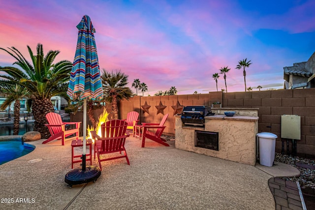 patio terrace at dusk featuring area for grilling and a fire pit