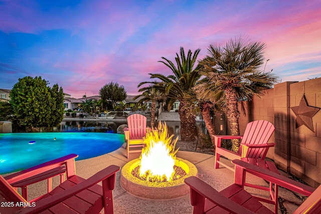 pool at dusk with a patio area, a water view, and an outdoor fire pit