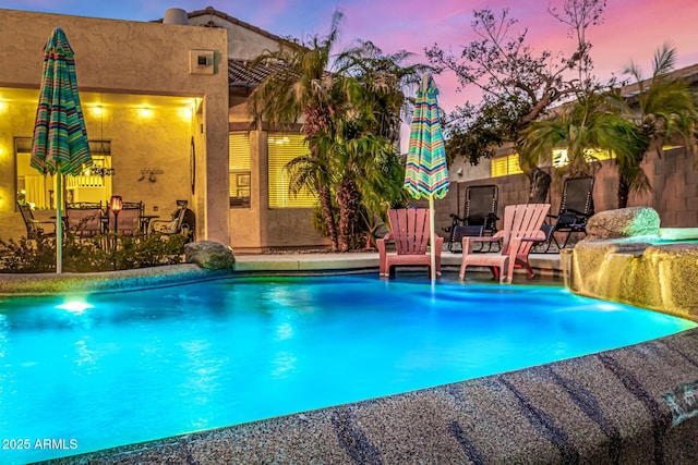 pool at dusk featuring pool water feature and a patio