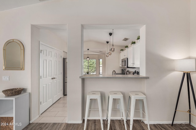 kitchen featuring stainless steel appliances, lofted ceiling, white cabinetry, and light wood-type flooring