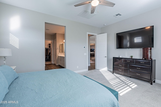 bedroom featuring ceiling fan, a spacious closet, light colored carpet, and ensuite bath