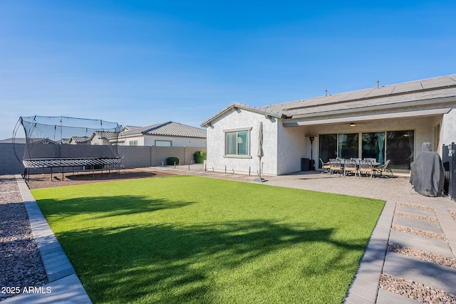 rear view of property with a patio area, a trampoline, and a lawn