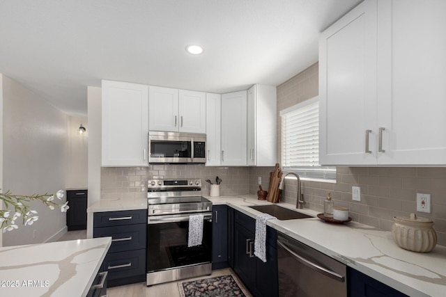 kitchen featuring light stone countertops, white cabinetry, appliances with stainless steel finishes, and a sink