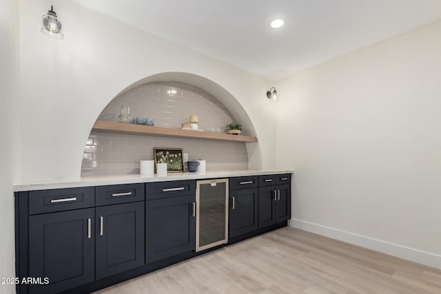 bar with light wood-style flooring, beverage cooler, baseboards, backsplash, and a dry bar