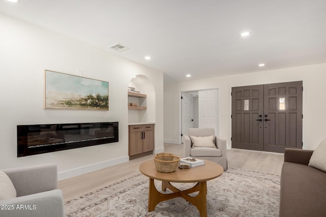 living room featuring light wood-type flooring, a glass covered fireplace, visible vents, and recessed lighting