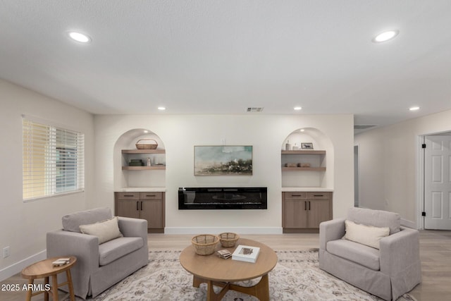 living room featuring baseboards, visible vents, built in features, a glass covered fireplace, and light wood-type flooring