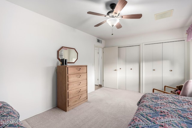 bedroom featuring light carpet, visible vents, and multiple closets