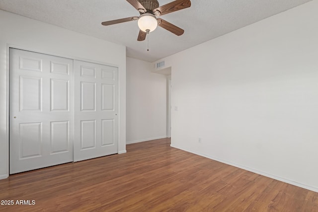 unfurnished bedroom with a textured ceiling, wood finished floors, visible vents, baseboards, and a closet