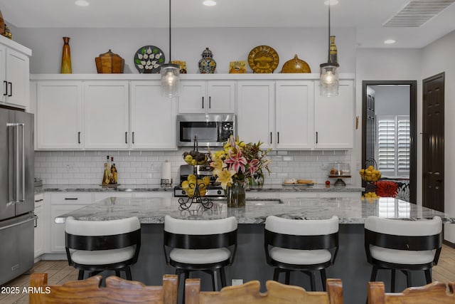 kitchen with stainless steel appliances, decorative backsplash, white cabinets, and hanging light fixtures