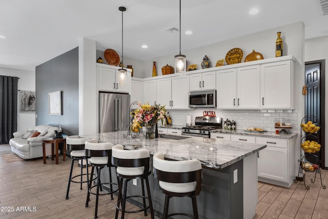 kitchen featuring a breakfast bar, hanging light fixtures, an island with sink, stainless steel appliances, and white cabinets