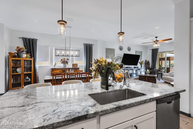 kitchen with pendant lighting, white cabinetry, sink, light stone counters, and stainless steel dishwasher