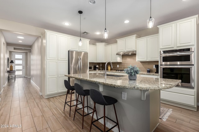 kitchen with white cabinets, an island with sink, appliances with stainless steel finishes, and hanging light fixtures