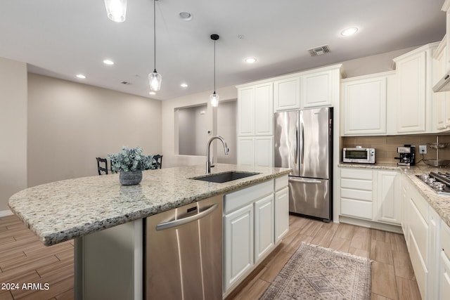 kitchen with an island with sink, appliances with stainless steel finishes, sink, and white cabinetry