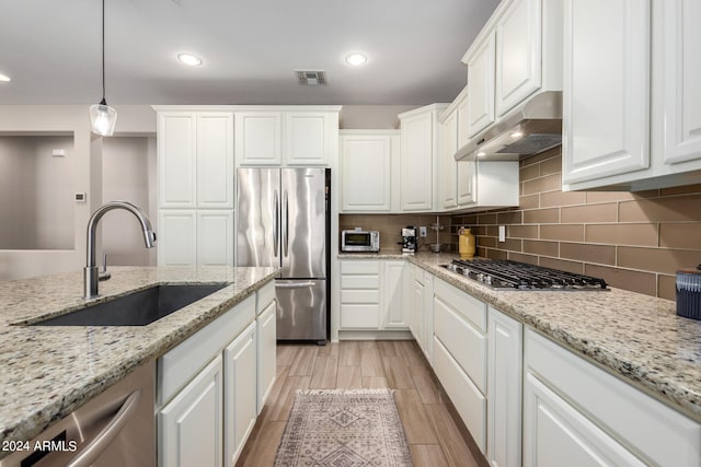 kitchen featuring pendant lighting, sink, light stone counters, appliances with stainless steel finishes, and white cabinetry