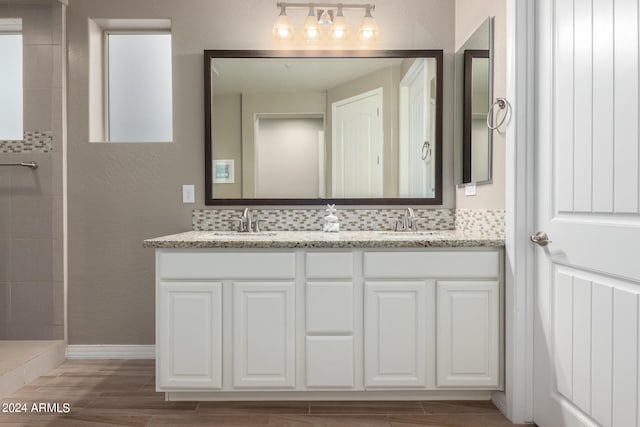 bathroom with hardwood / wood-style flooring, tiled shower, vanity, and tasteful backsplash