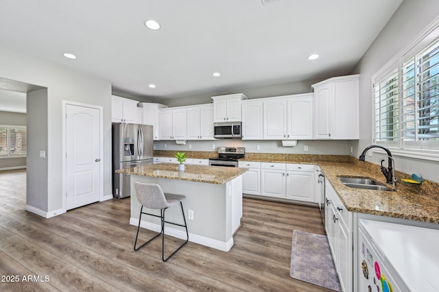 kitchen featuring recessed lighting, appliances with stainless steel finishes, wood finished floors, white cabinetry, and a sink