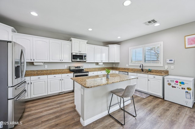 kitchen with wood finished floors, visible vents, a sink, white cabinets, and appliances with stainless steel finishes