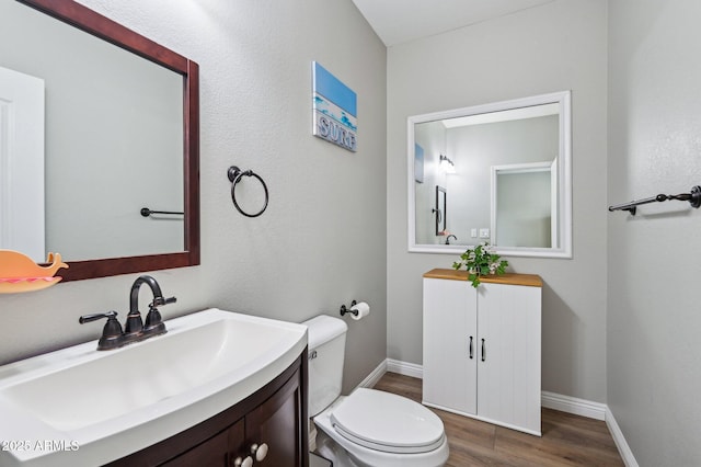 half bath featuring vanity, toilet, wood finished floors, and baseboards