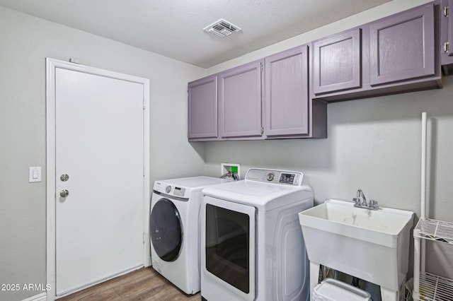 laundry area featuring visible vents, washing machine and clothes dryer, cabinet space, a sink, and light wood-style floors