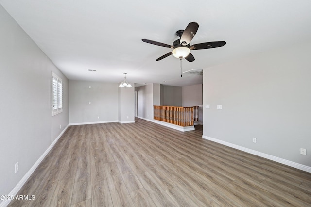 unfurnished living room with visible vents, light wood finished floors, baseboards, and ceiling fan with notable chandelier