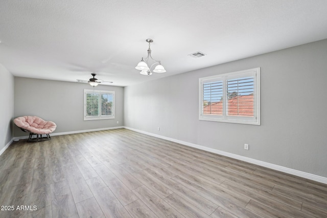 spare room featuring visible vents, ceiling fan with notable chandelier, baseboards, and wood finished floors