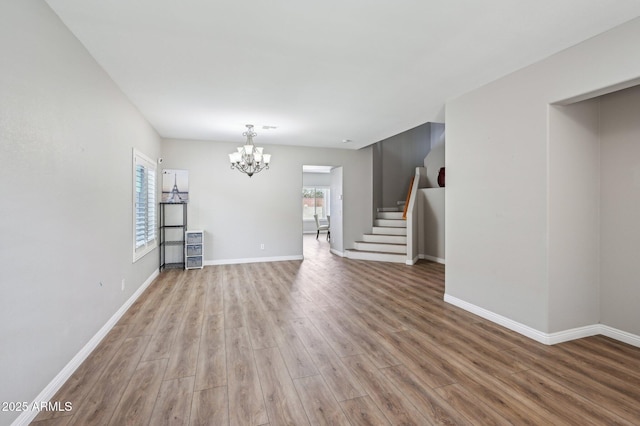 unfurnished living room featuring stairway, baseboards, an inviting chandelier, and wood finished floors