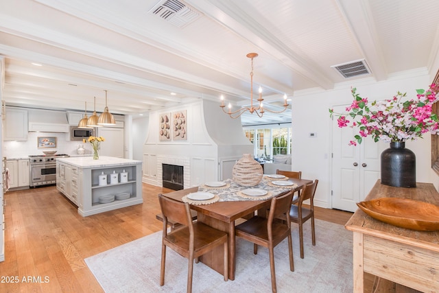 dining area featuring visible vents, beamed ceiling, a fireplace, and light wood finished floors