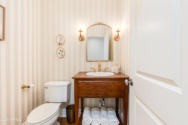 half bath featuring wallpapered walls, toilet, and vanity